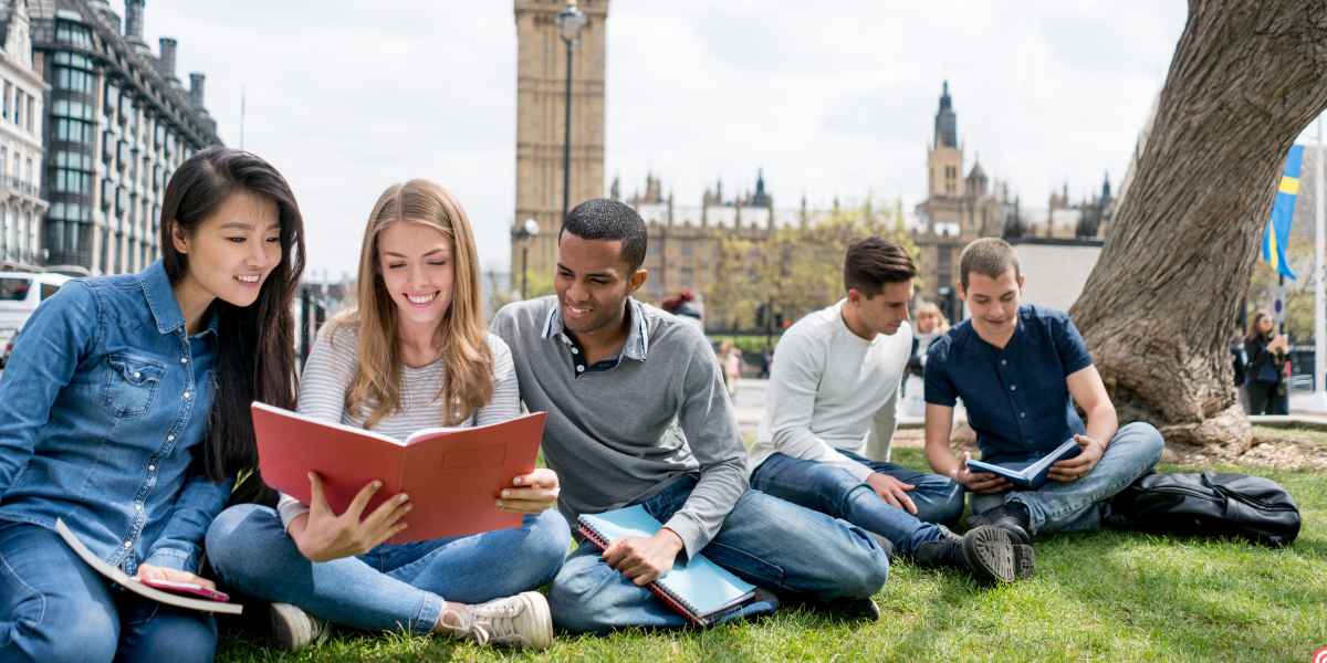 A diverse group of university students sitting on the grass in a London park, reading notebooks and studying together with the Elizabeth Tower (Big Ben) in the background.